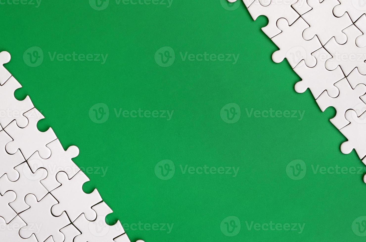 Fragment of a folded white jigsaw puzzle on the background of a green plastic surface. Texture photo with copy space for text