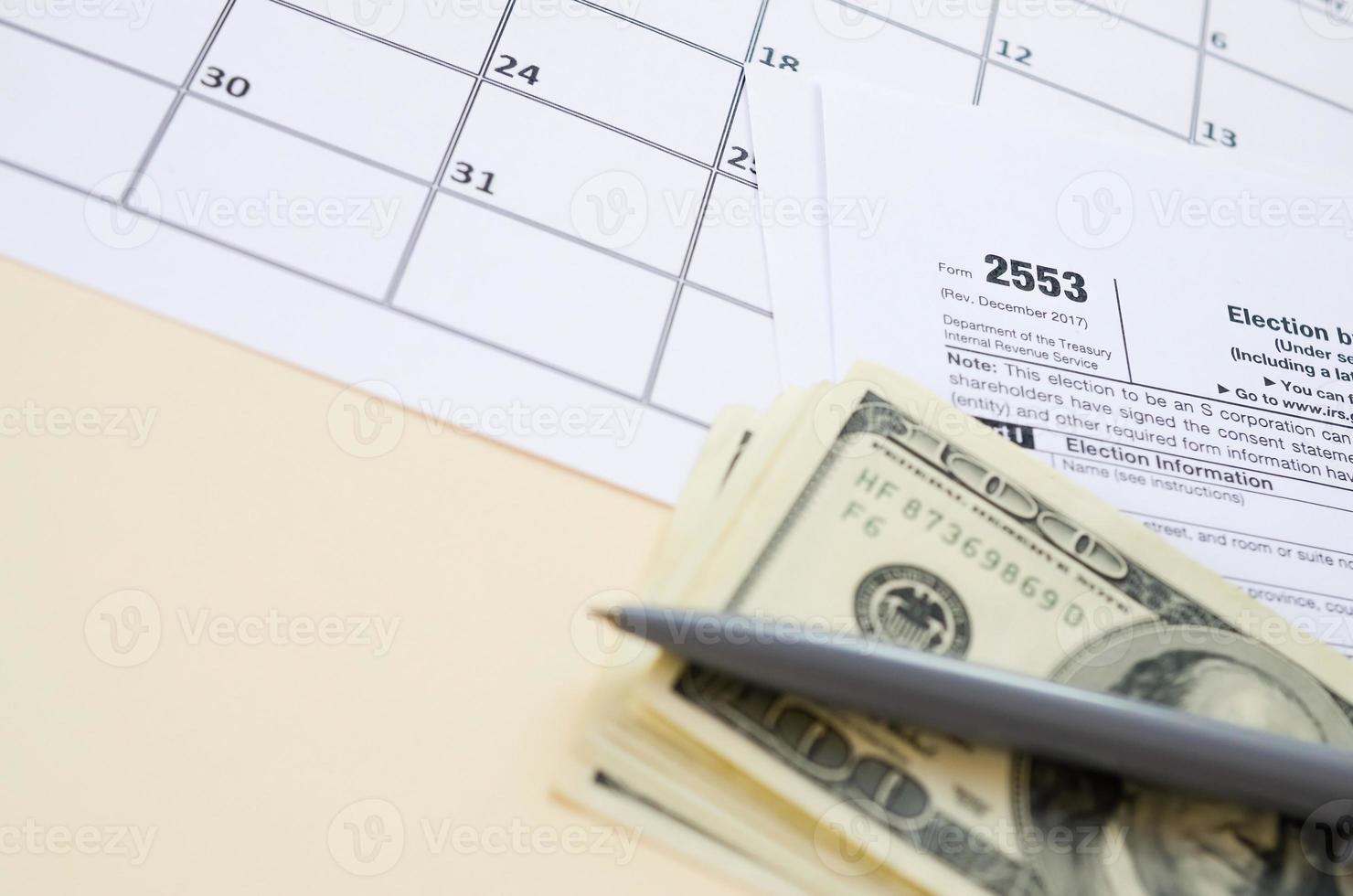 irs form 2553 elección por un impuesto de sociedades de pequeñas empresas en blanco se encuentra con bolígrafo y muchos billetes de cien dólares en la página del calendario foto