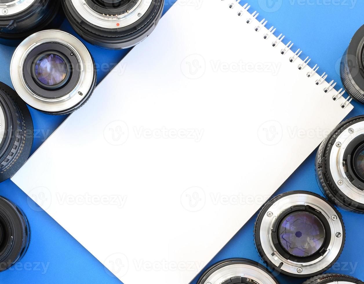 Several photographic lenses and white notebook lie on a bright blue background. Space for text photo