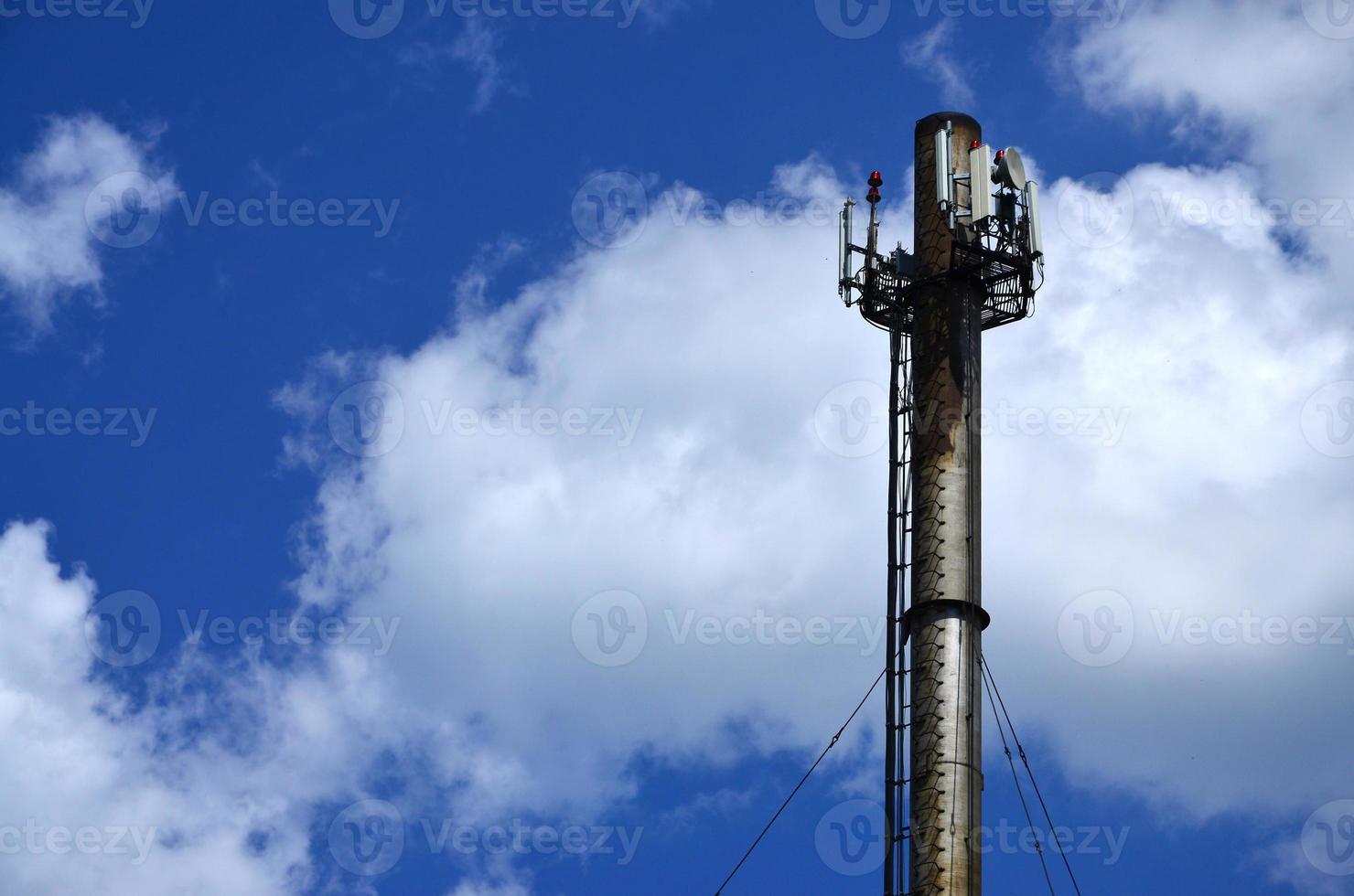 High metal chimney of industrial plant with ladder in the form of metal braces against the background of a cloudy blue sky photo