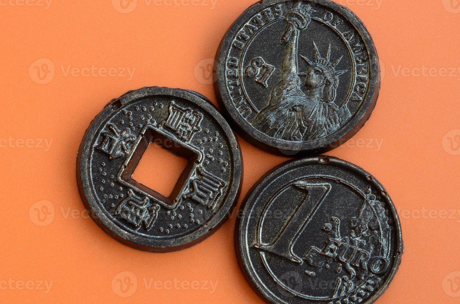Three chocolate products in the form of Euro, USA and Japan coins lie on an orange plastic background. A model of cash coins in an edible form photo