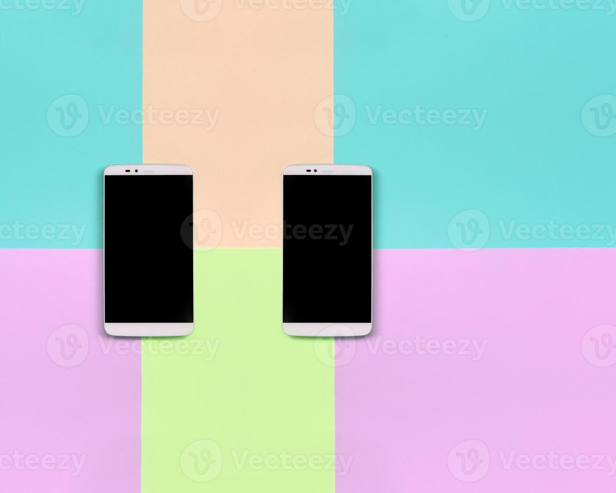 Two modern smartphones with black screens on background of fashion pastel pink, blue, coral and lime colors photo