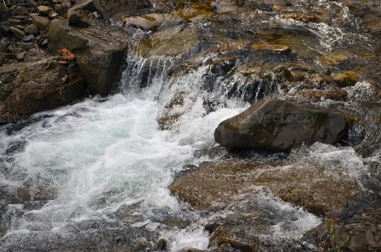 imagen de primer plano de una pequeña cascada salvaje en forma de corrientes cortas de agua entre piedras de montaña foto