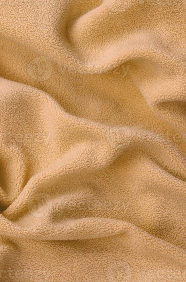 The blanket of furry orange fleece fabric. A background of light orange soft plush fleece material with a lot of relief folds photo