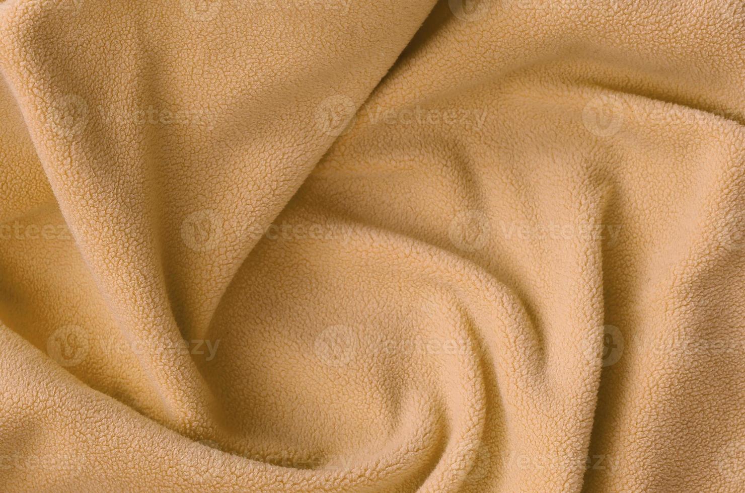 The blanket of furry orange fleece fabric. A background of light orange soft plush fleece material with a lot of relief folds photo