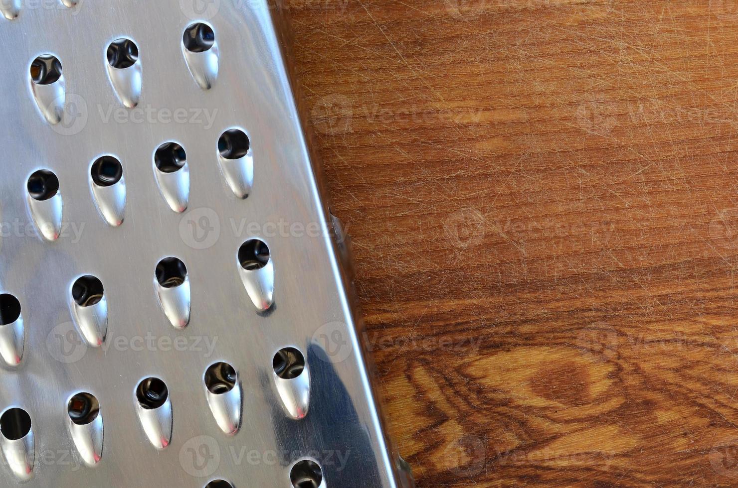 el rallador de cromo se encuentra en la tabla de cortar con muchas cicatrices del hacha y el cuchillo. imagen de fondo para recetas de cocina foto