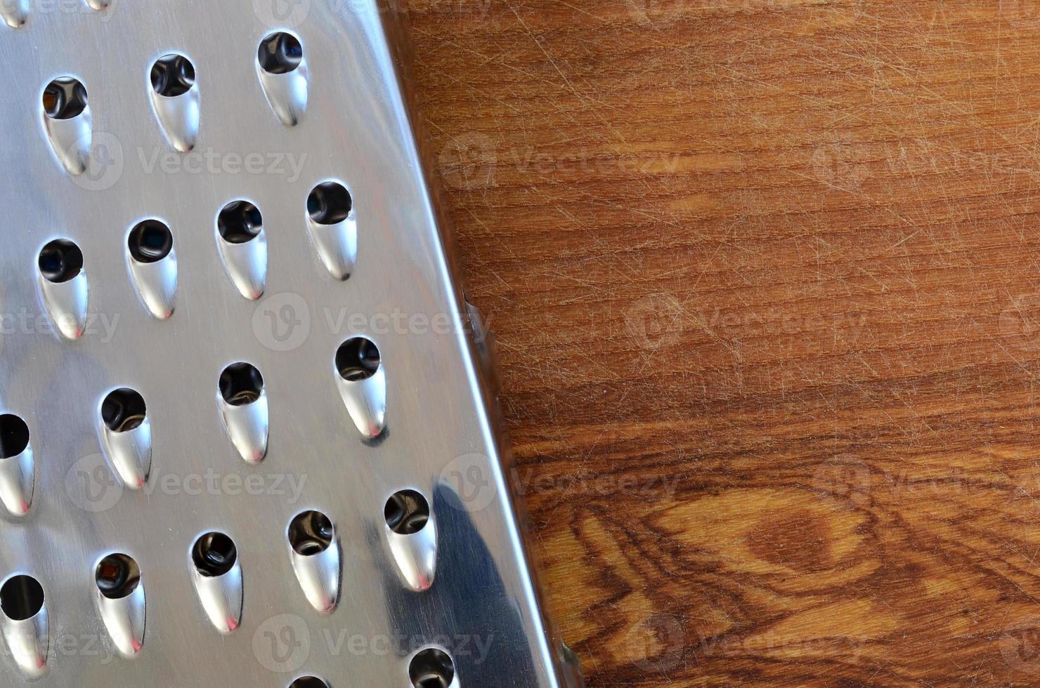 The chrome grater lies on the cutting board with a lot of scars from the ax and knife. Background image for cooking recipes photo