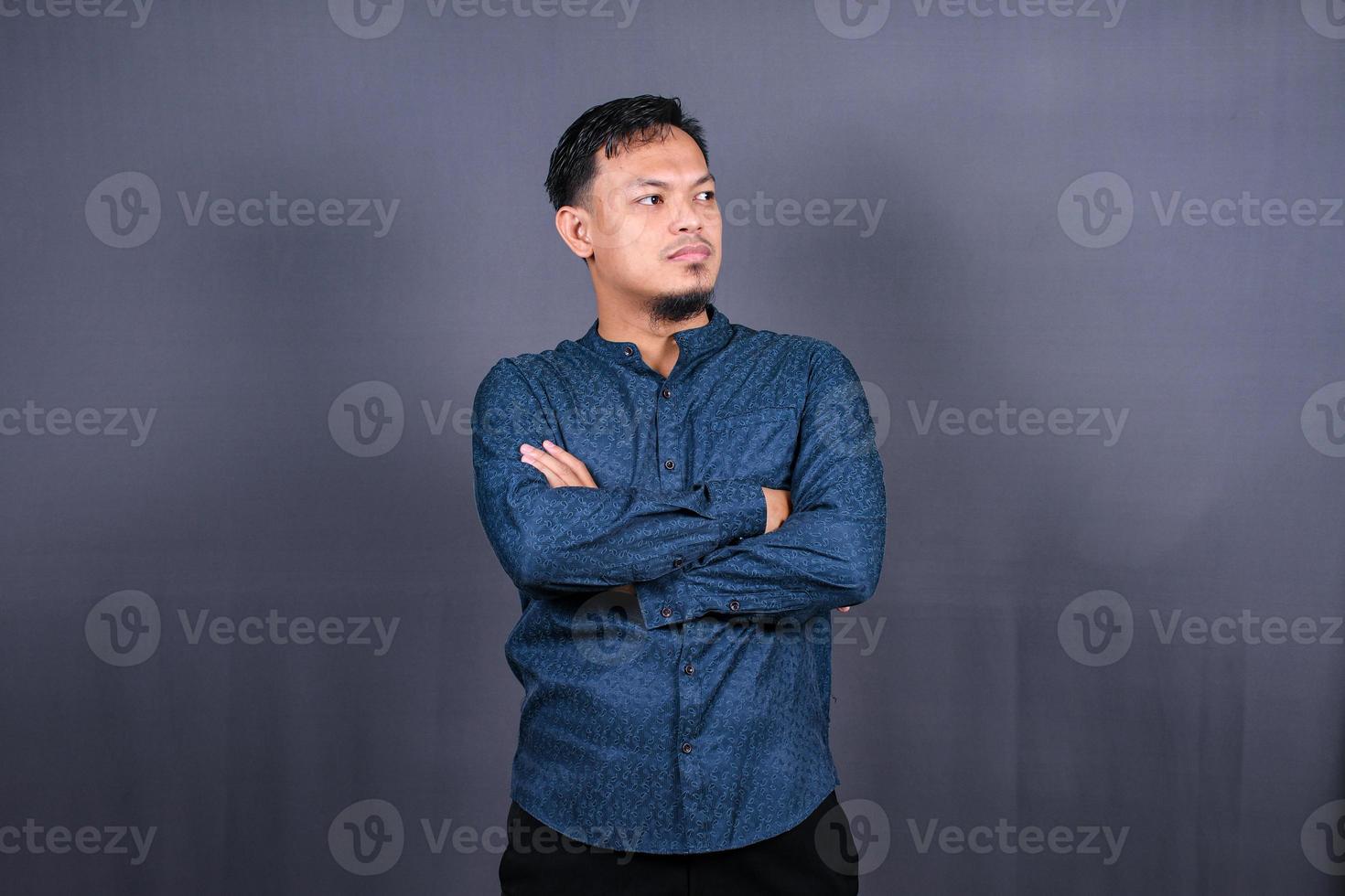 Smiling Asian man with blue shirt standing with hands folded isolated on grey background. Concept of engineering jobs photo
