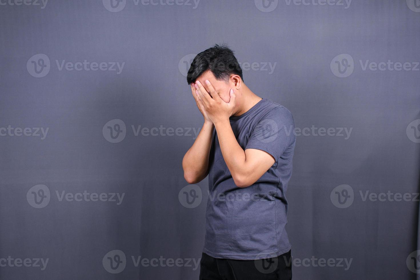 Depressed Asian Young man having stressful time with hands covering face. isolated on gray background. photo