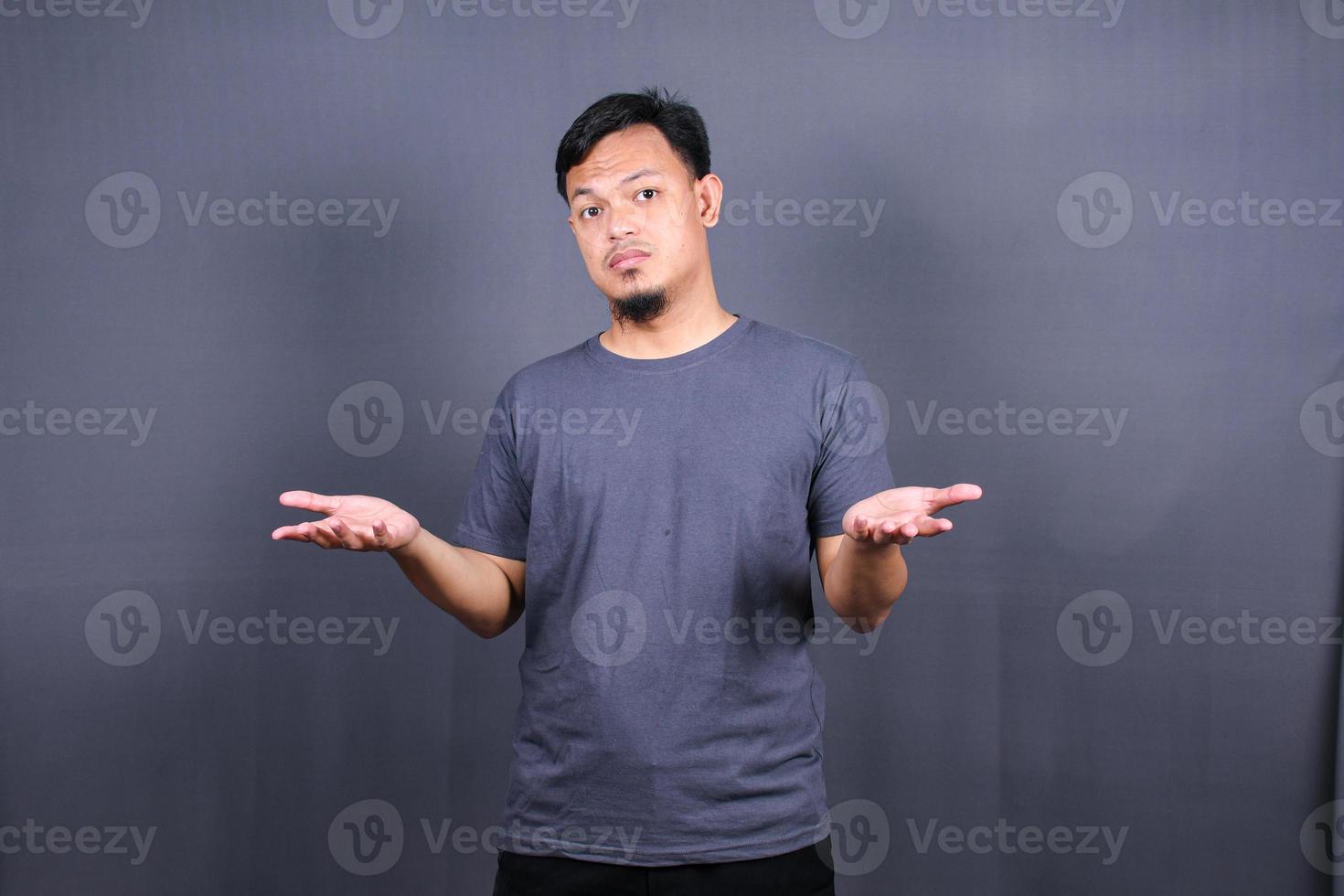 Closeup portrait of clueless funny looking young asian man, arms out asking what do I do now or gesturing I don't know, isolated on gray background. photo