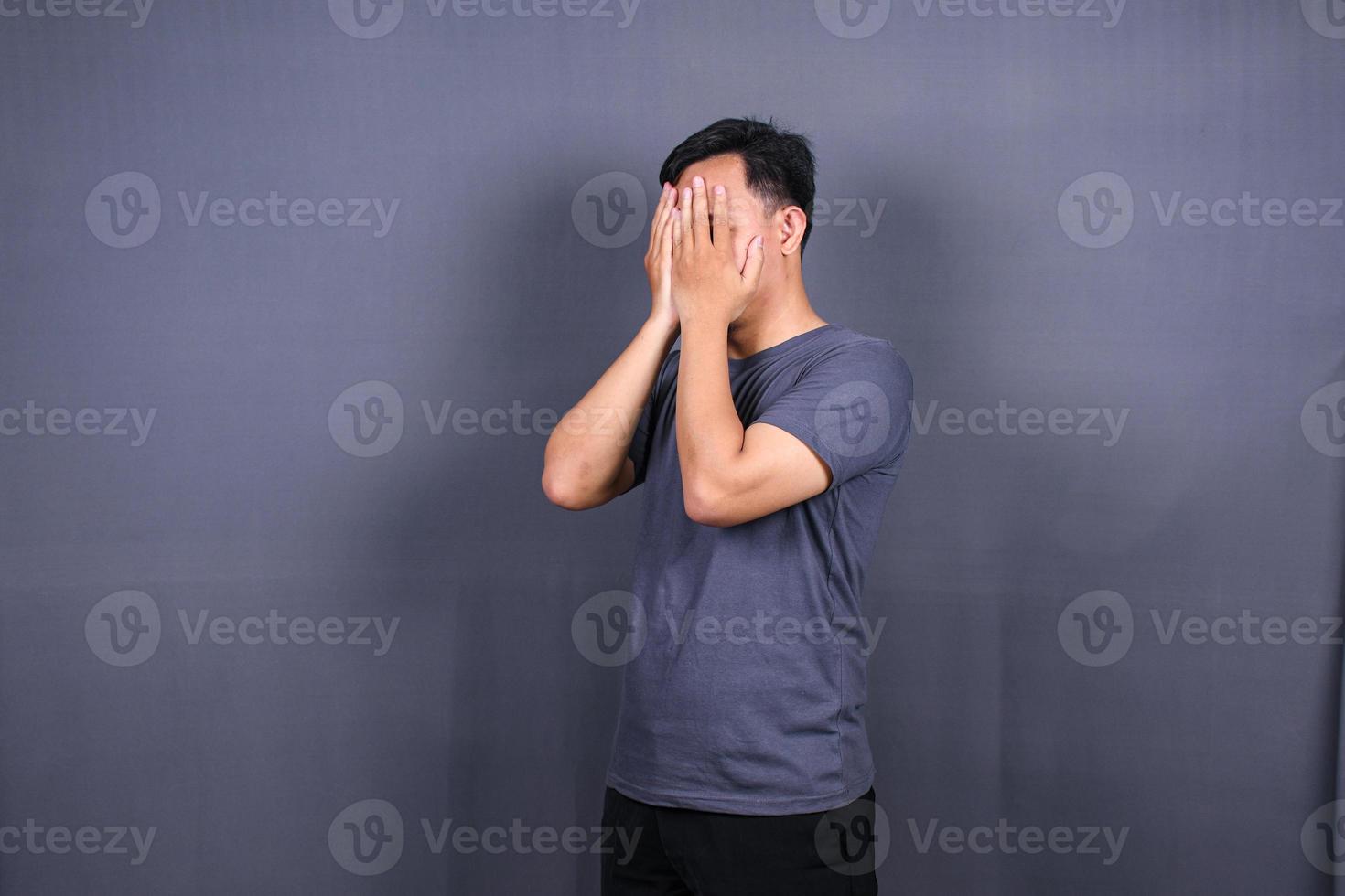 Depressed Asian Young man having stressful time with hands covering face. isolated on gray background. photo