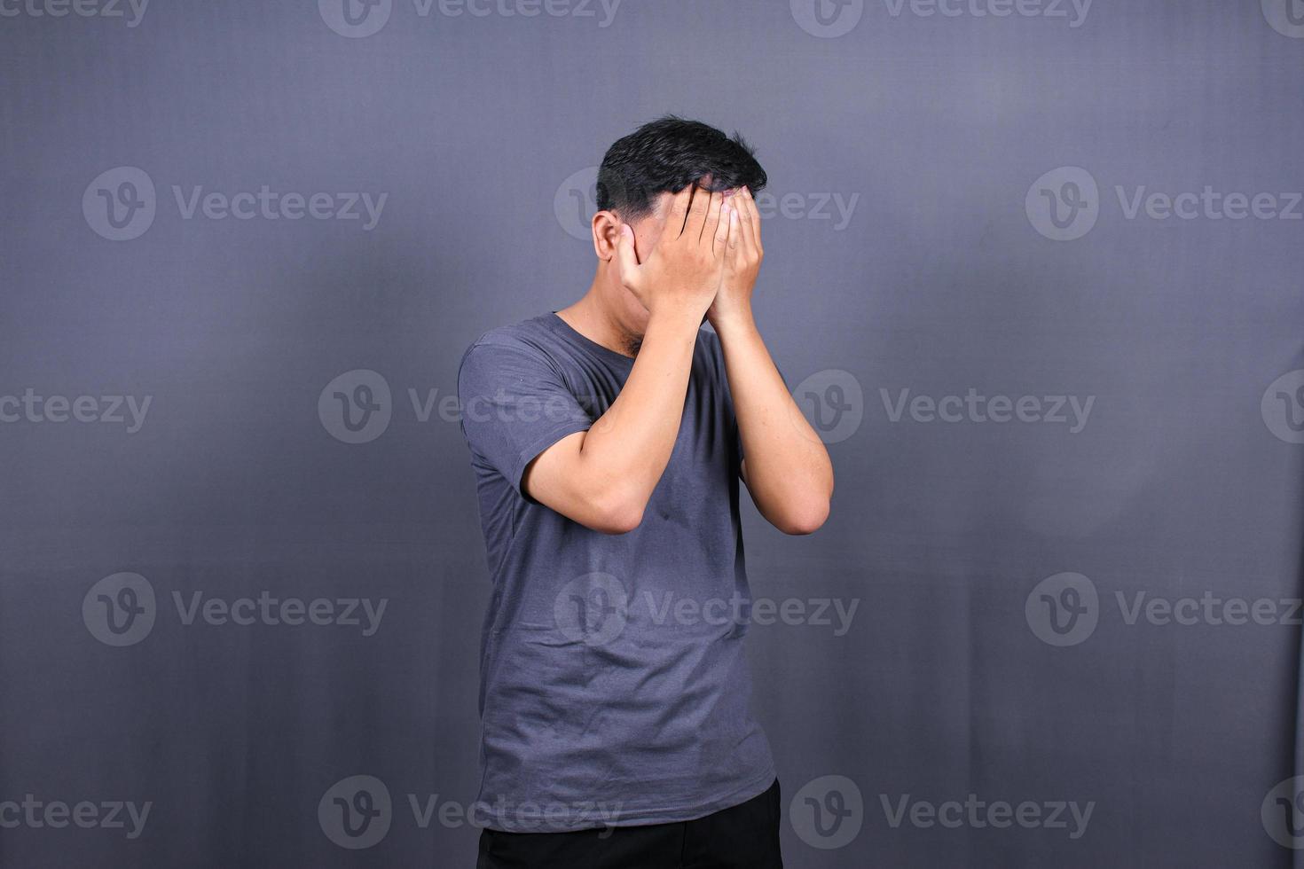 Depressed Asian Young man having stressful time with hands covering face. isolated on gray background. photo