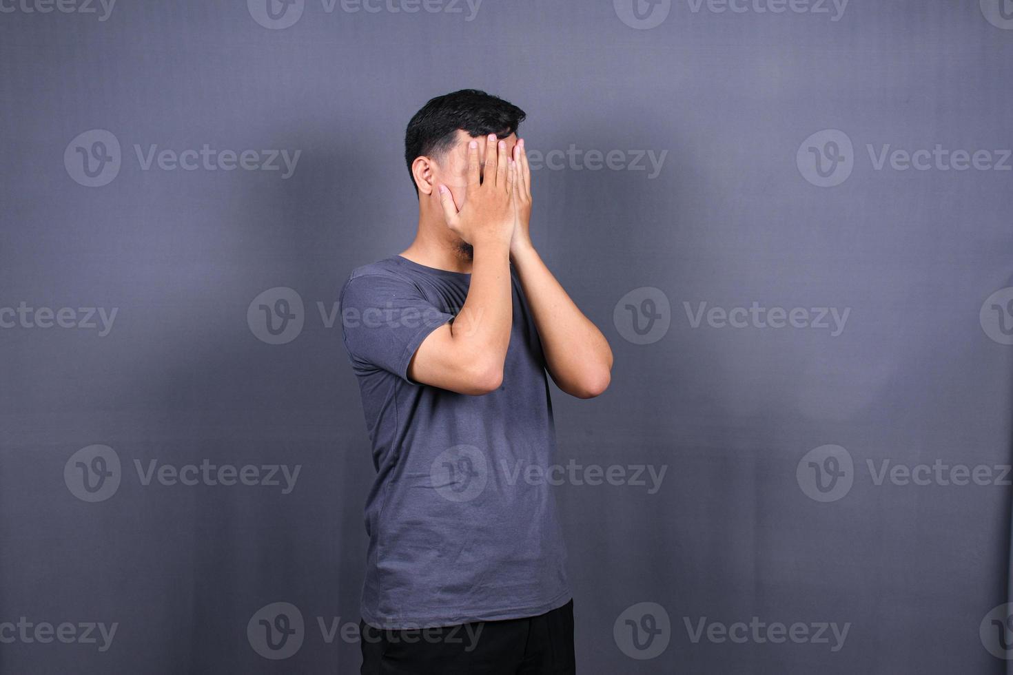 Depressed Asian Young man having stressful time with hands covering face. isolated on gray background. photo