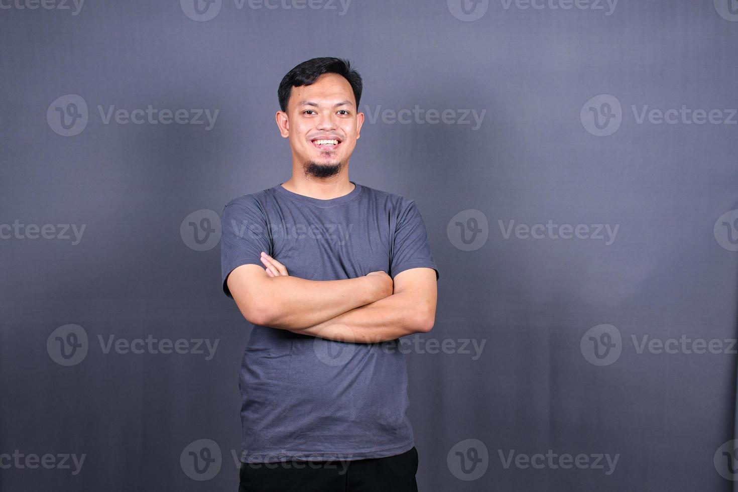 Smiling handsome man in gray t-shirt standing with crossed arms isolated on gray background photo