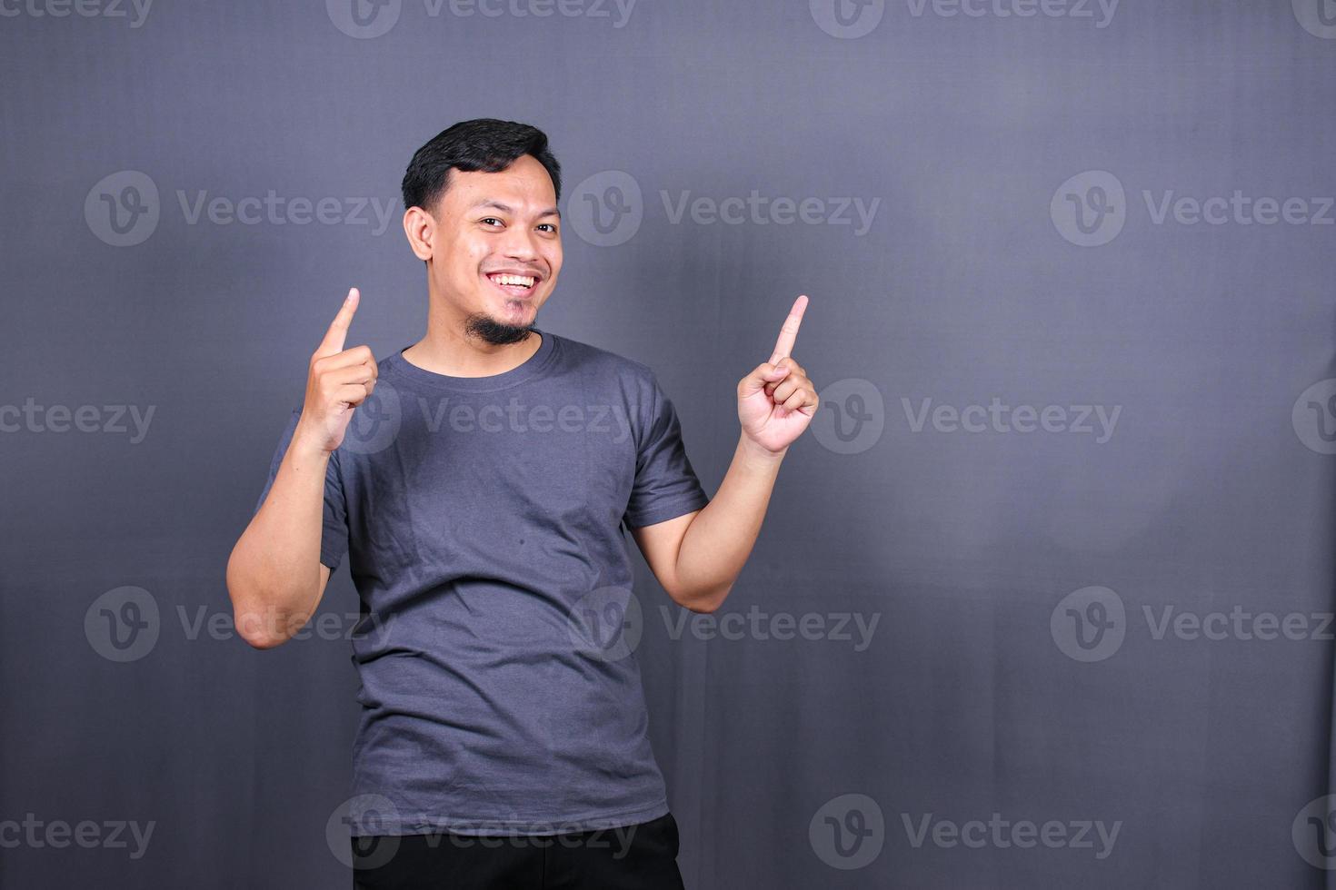 Young attractive smiling asian man in tshirt posing isolated on gray background, Mock up copy space. photo