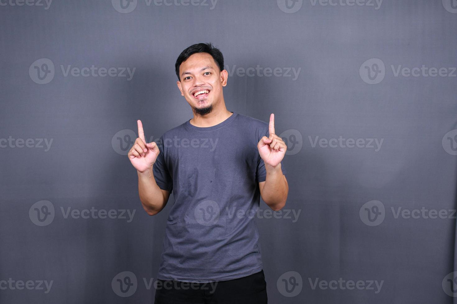 Young attractive smiling asian man in tshirt posing isolated on gray background, Mock up copy space. photo