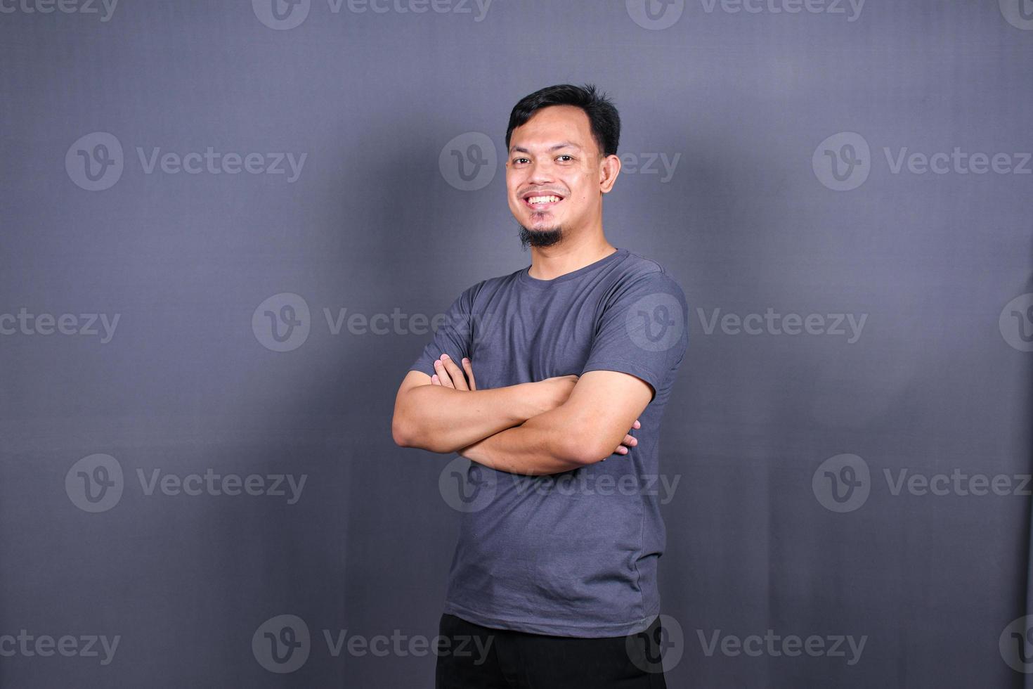 Smiling handsome man in gray t-shirt standing with crossed arms isolated on gray background photo