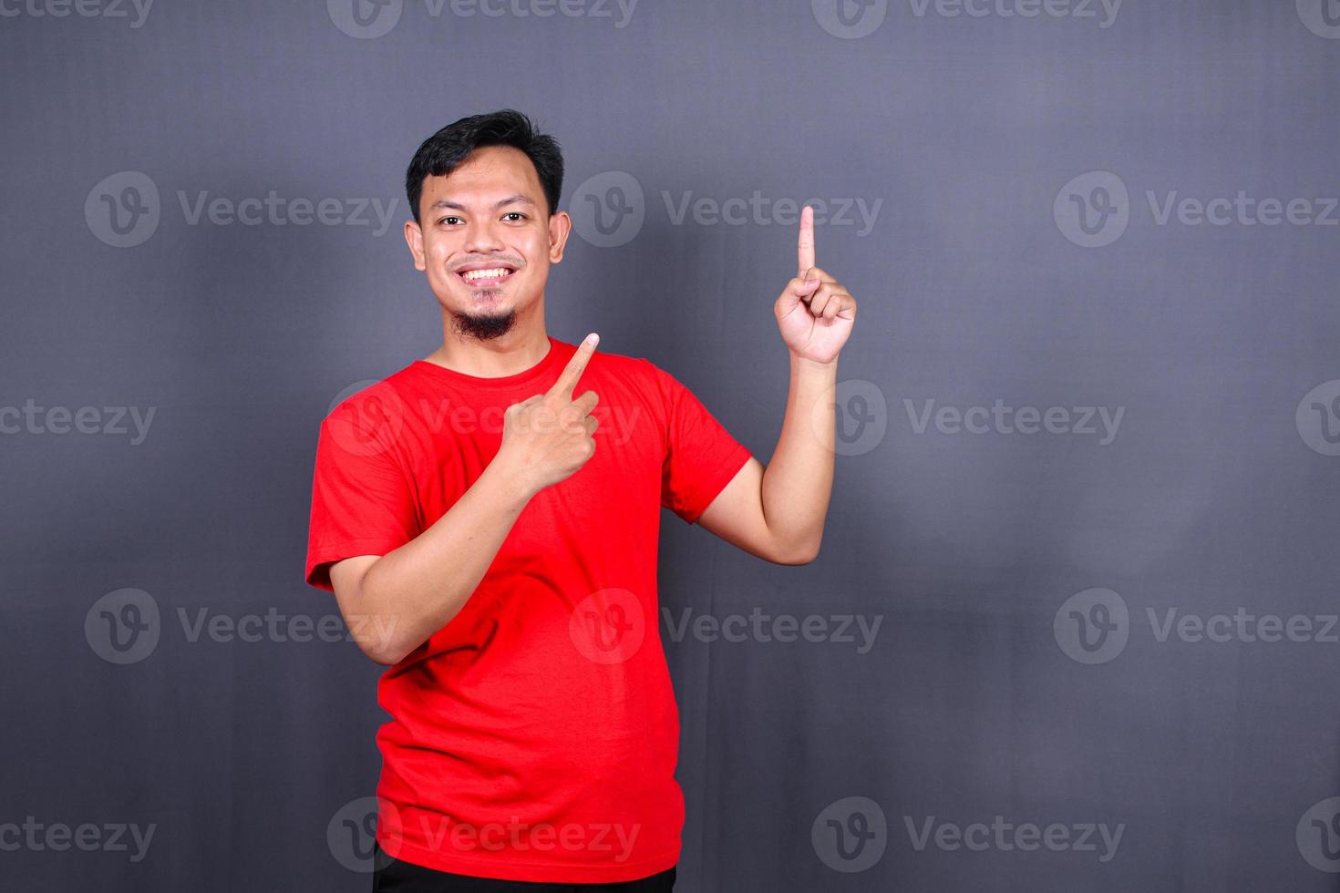 Asian young man in red t-shirt pointing with his finger isolated on gray background photo