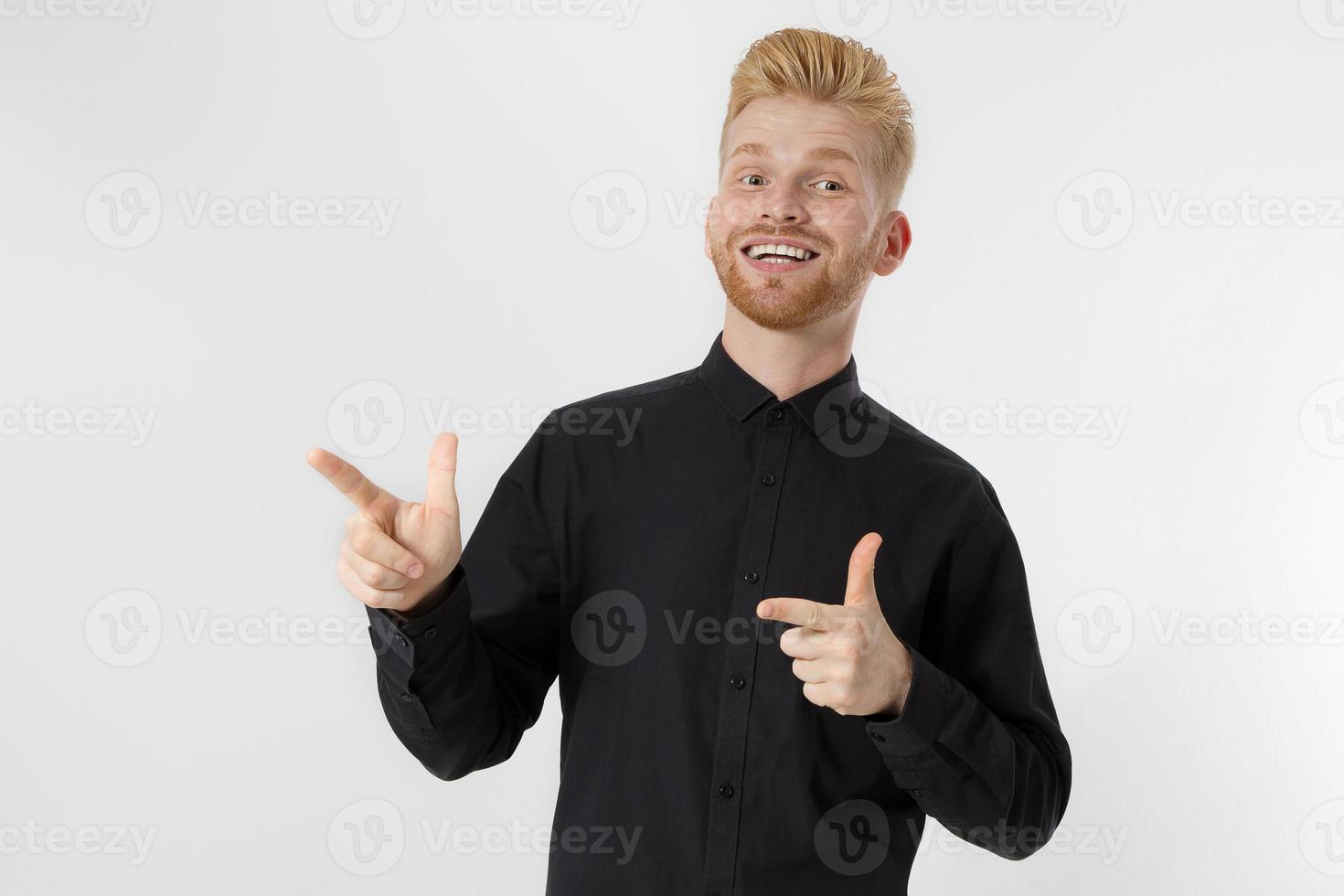 Happy young redhead guy with red stylish beard isolated. Man pointing copy space for advertising. Male in black shirt, trend haircut. Successful young entrepreneur. Surprised shocked excited man face photo