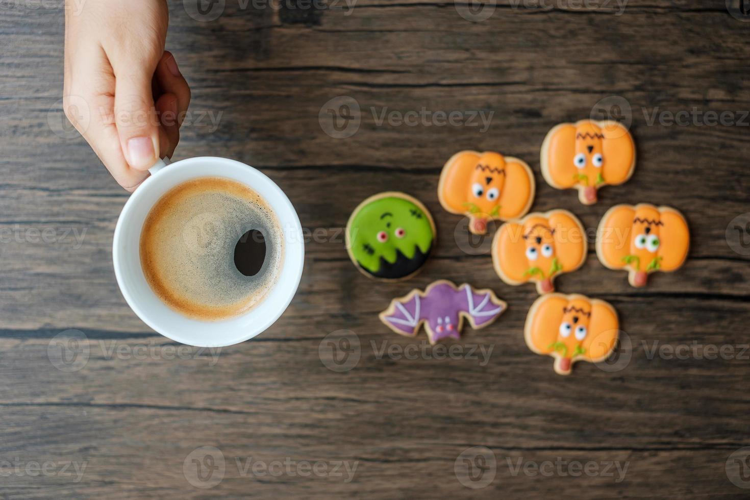 hand holding coffee cup during eating funny Halloween Cookies. Happy Halloween day, Trick or Threat, Hello October, fall autumn, Traditional, party and holiday concept photo