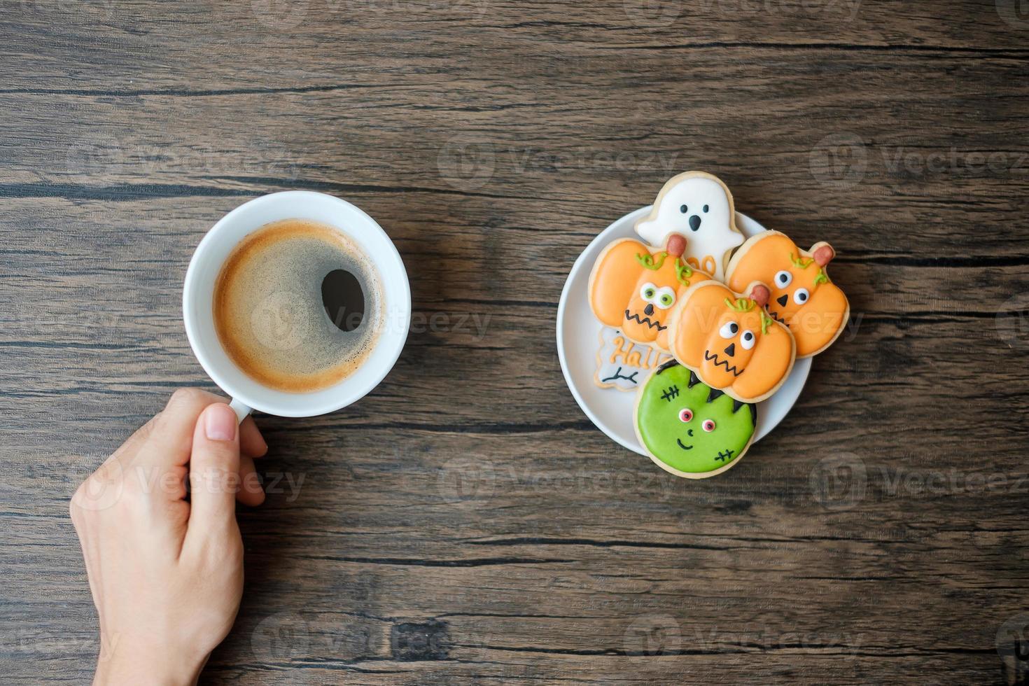 hand holding coffee cup during eating funny Halloween Cookies. Happy Halloween day, Trick or Threat, Hello October, fall autumn, Traditional, party and holiday concept photo