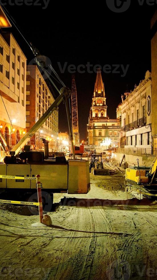 Construction at night, heavy machinery, backhoe, grader, road roller, a church in the background photo