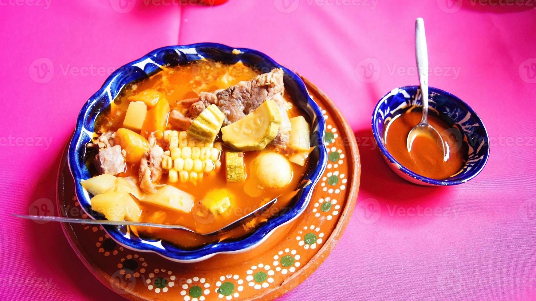 clay plate with pozole, traditional Mexican food, pink tablecloth, metal spoon photo