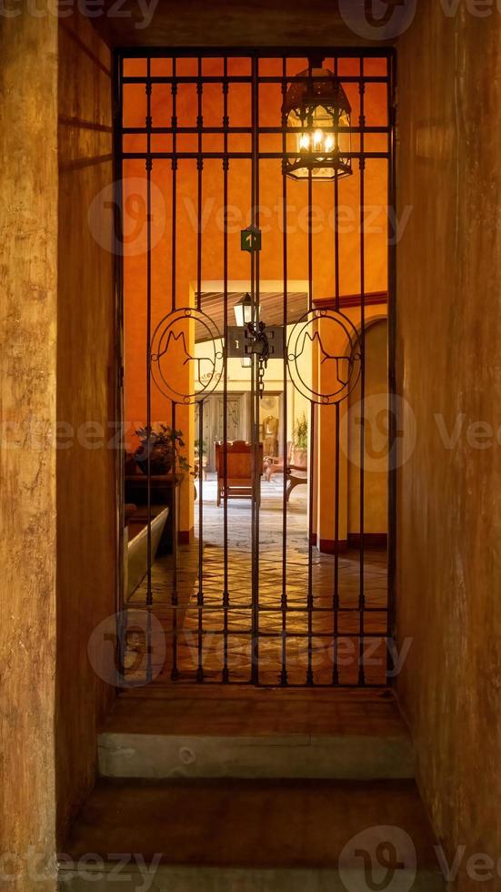 entrada a una casa antigua, detrás de una lámpara de araña encendida, suelo de piedra y paredes de hormigón, luz naranja en el espacio, méxico foto