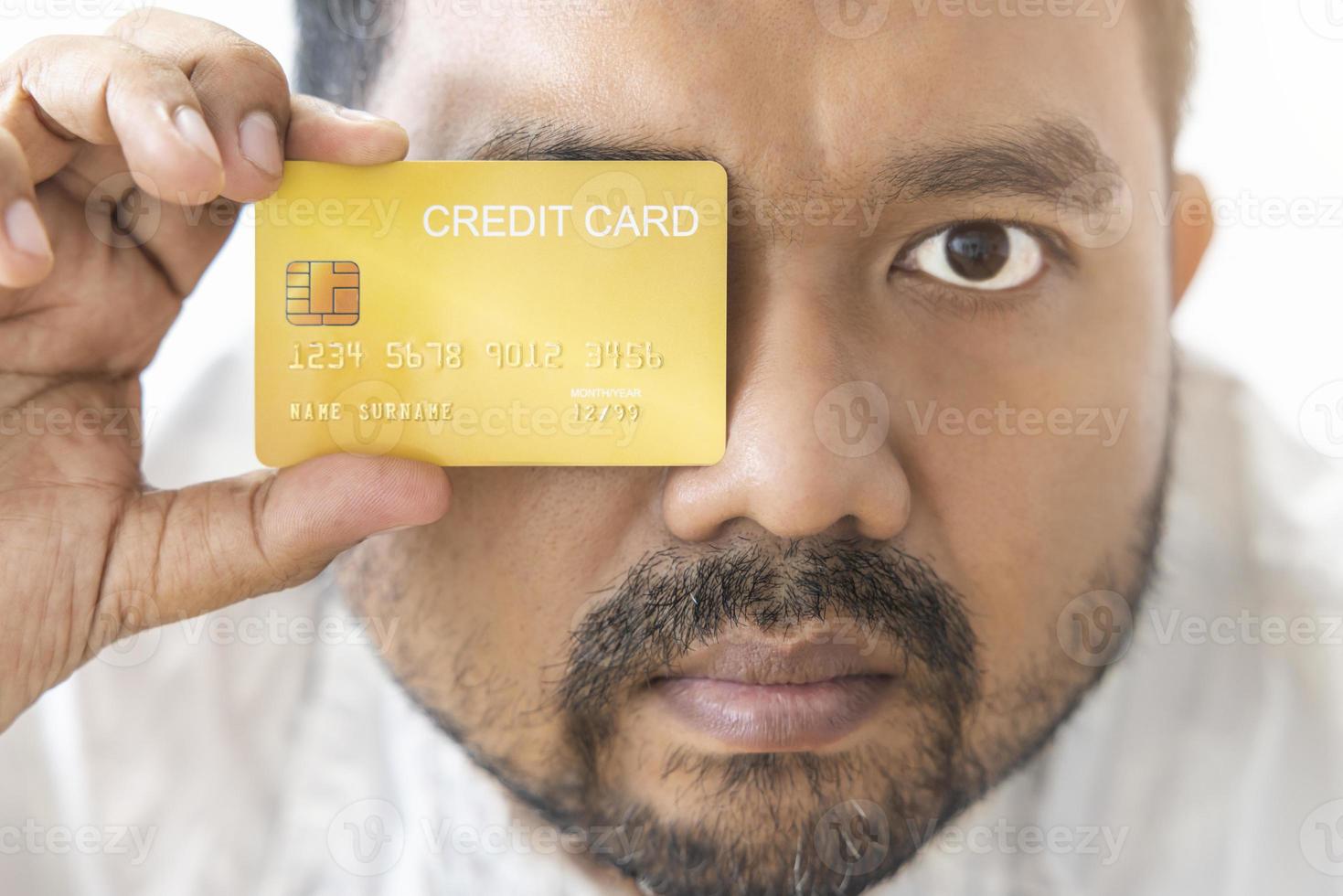 Close-up of Asian man holding yellow gold credit card in his hand close the right eye isolated on white background. Concept of trading, social, technology, business photo