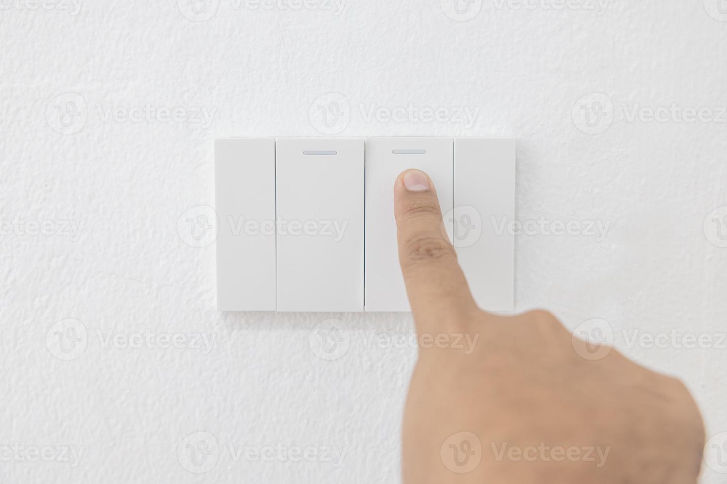 Close-up light switch of a male finger will turn on or off a light switch with white wall at home. white plastic mechanical switch mounted. Energy, energy, save electricity, copy space photo