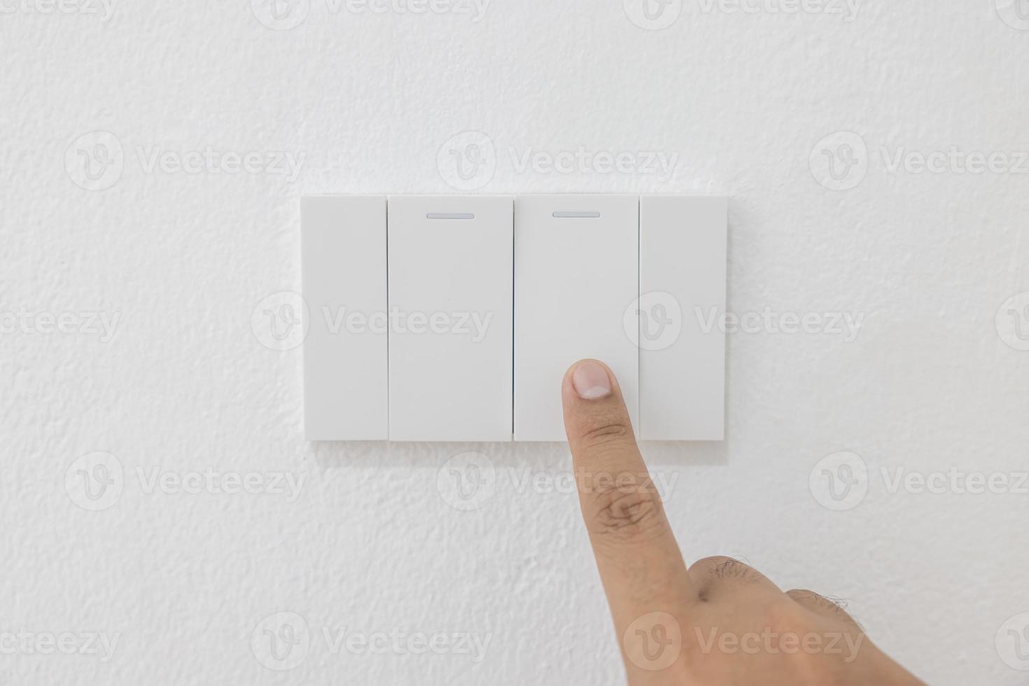 Close-up light switch of a male finger will turn on or off a light switch with white wall at home. white plastic mechanical switch mounted. Energy, energy, save electricity, copy space photo