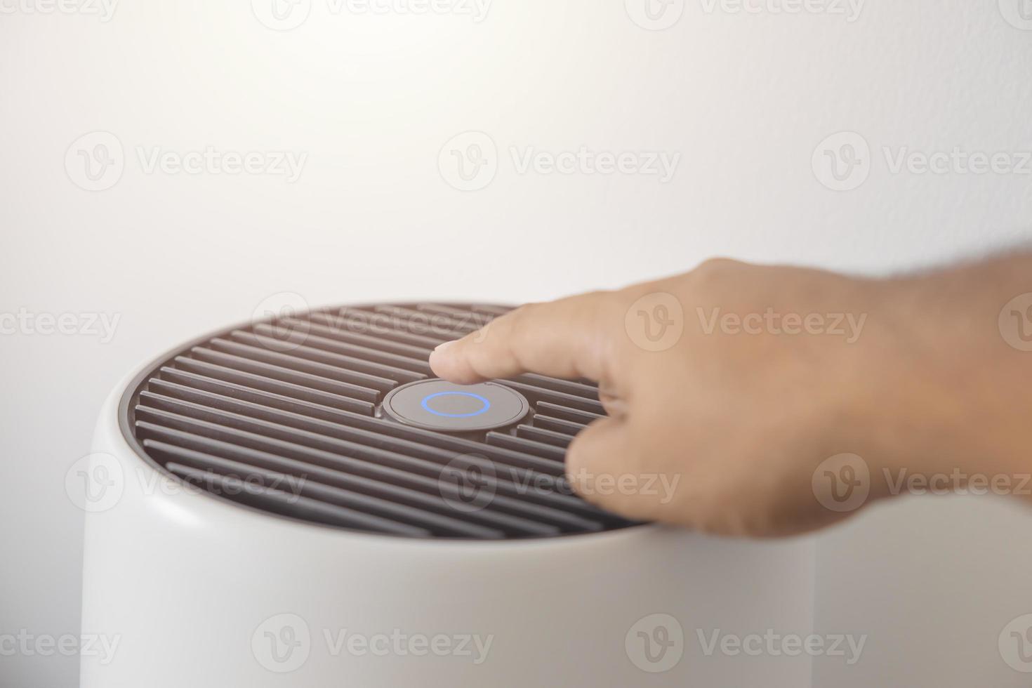 mano de hombre asiático de primer plano, presionando un botón en la máquina purificadora de aire en un dormitorio. proteger el concepto de contaminación del aire y el polvo pm 2.5. filtro de aire que quita el polvo fino en casa foto