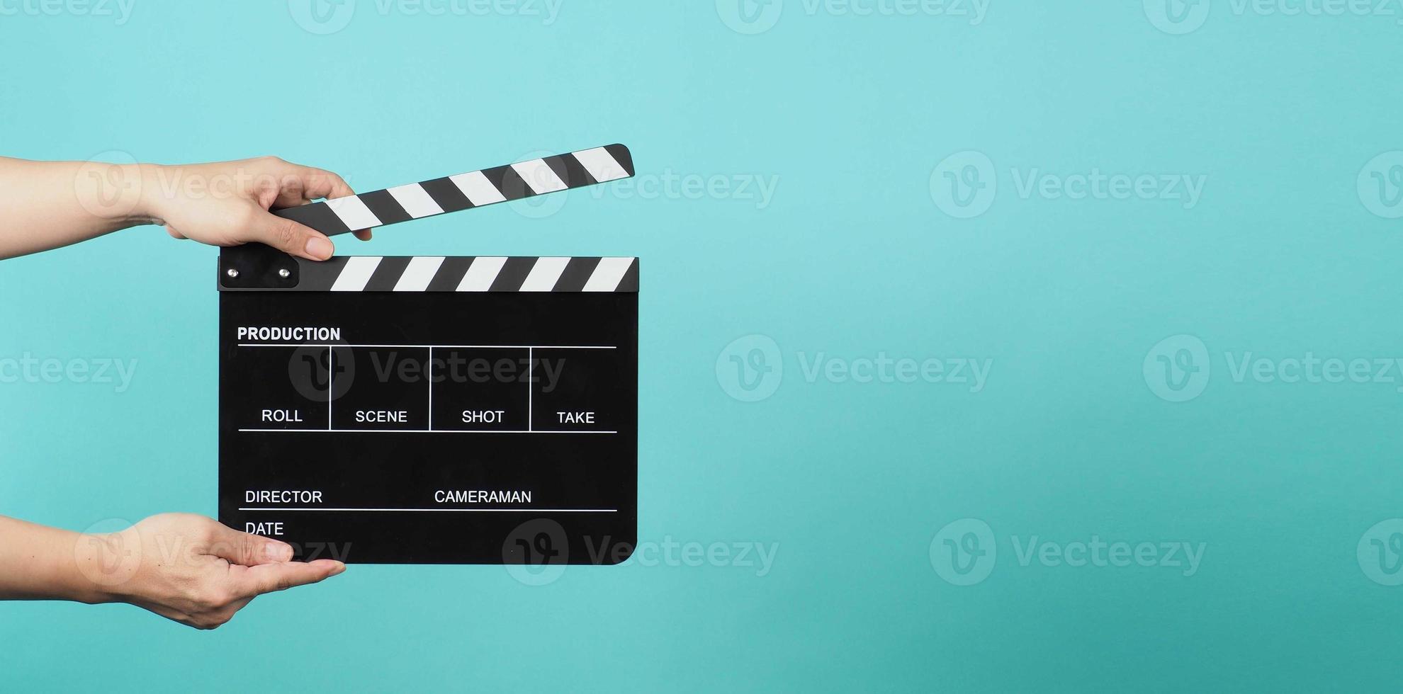 Hand is holding Black clapper board or movie slate on green or mint or Tiffany Blue background. photo