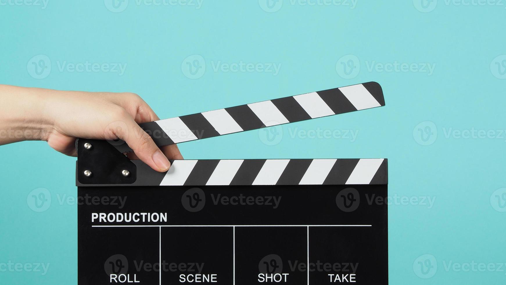 Hand is holding Black clapper board or movie slate on green or Turquoise background. photo