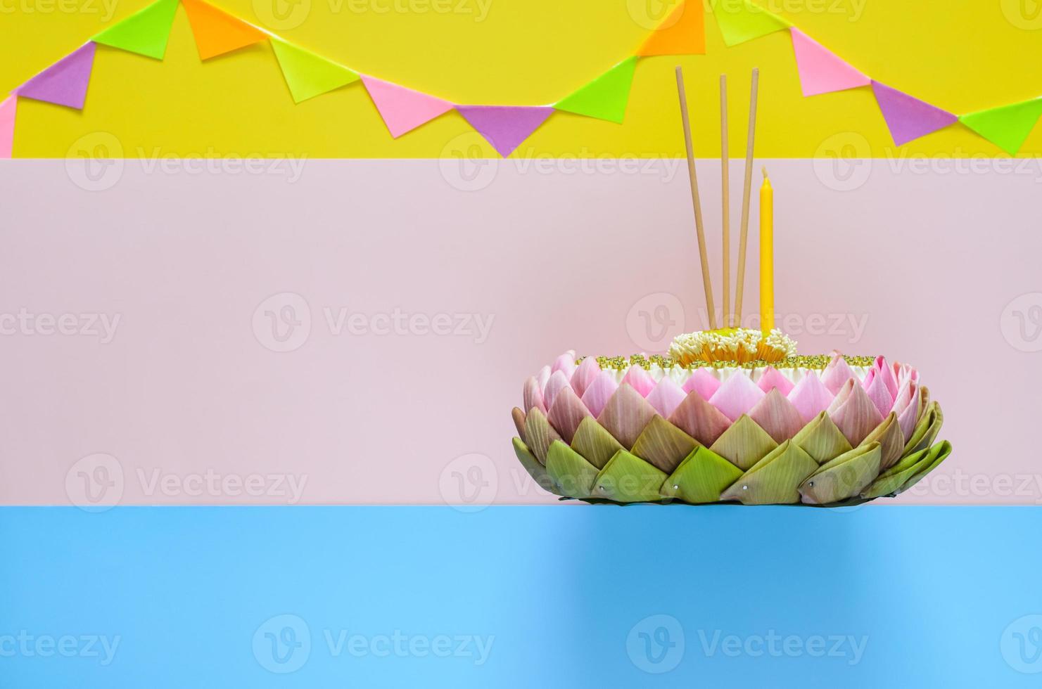 Selective focus at lotus pollen on top of pink lotus petal krathong with crown flower, incense stick and candle for Thailand Loy Krathong festival on colorful background with party flag. photo