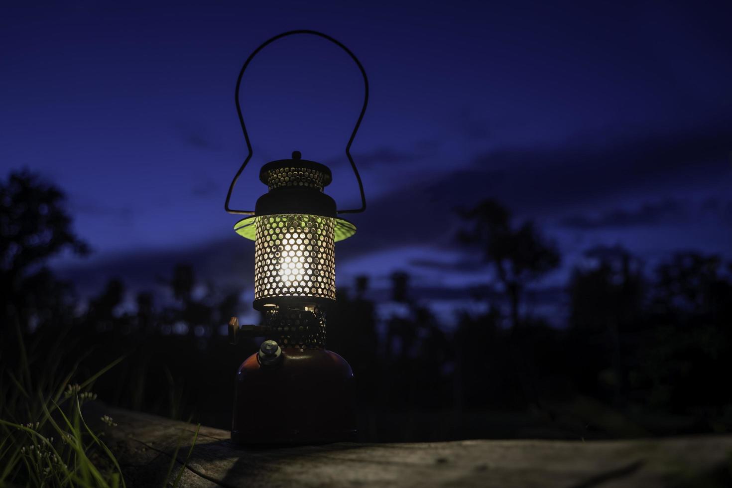 Ancient oil lamp lit on an old log. in the forest at night photo