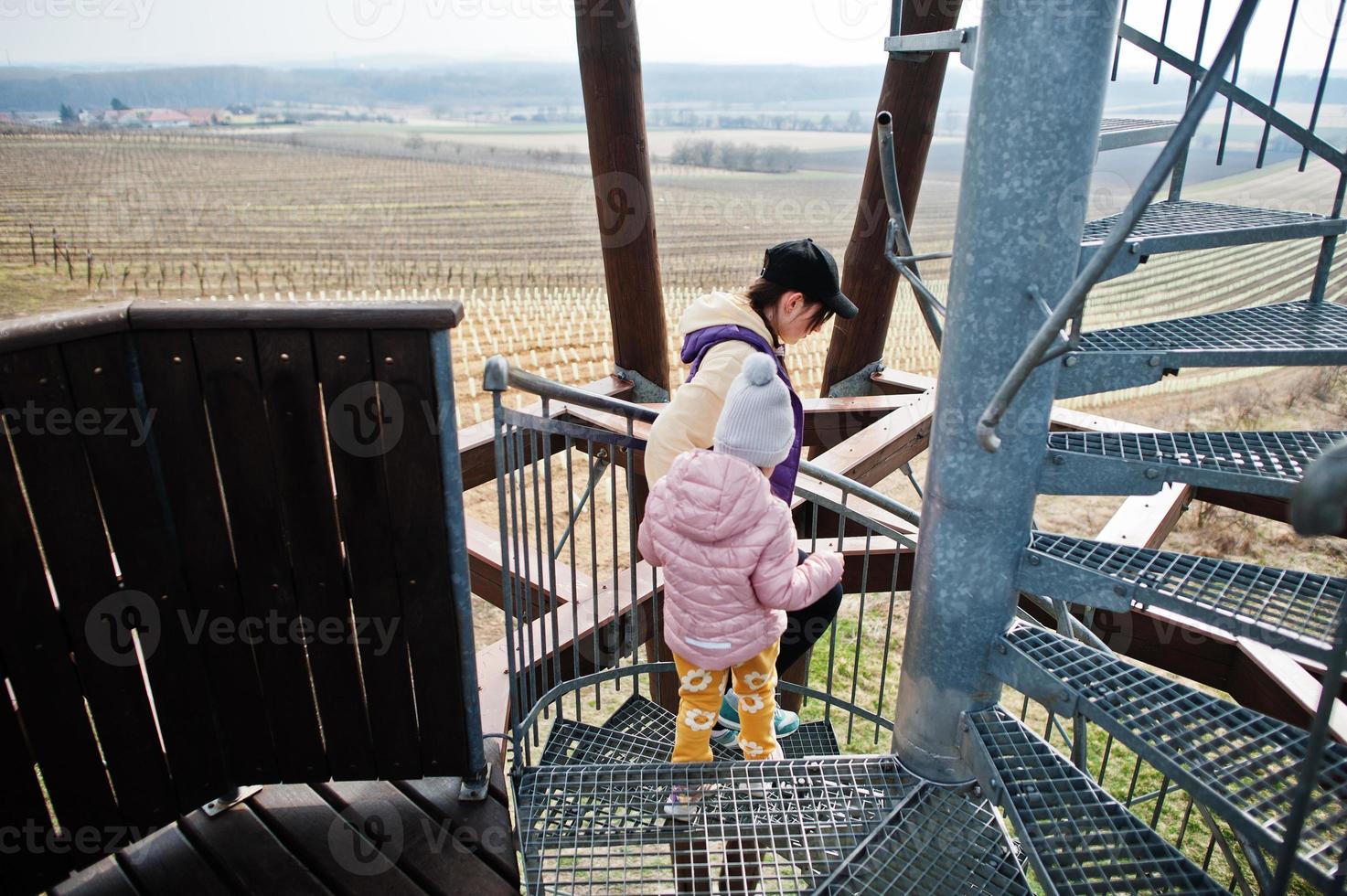 Mother with daughter stand at spiral staircase of wooden observation tower. photo