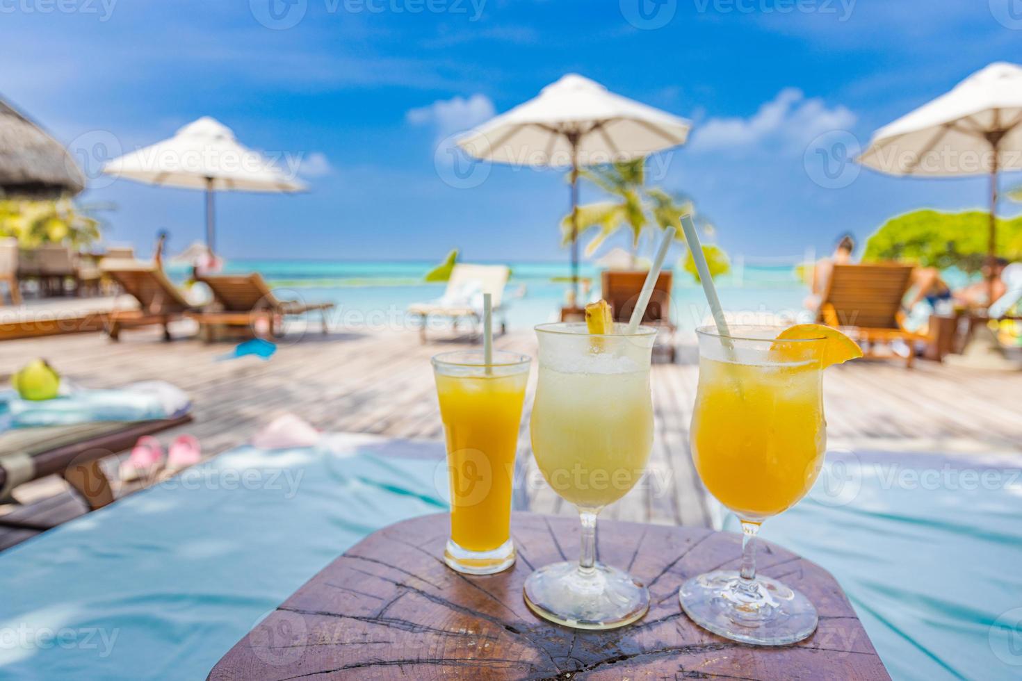 Colorful cocktails on luxury beach resort. Blurred poolside, chairs, beds under umbrella and palm tree leaves. Tropical island beachfront, infinity pool, summer vibes, cool drink glasses photo