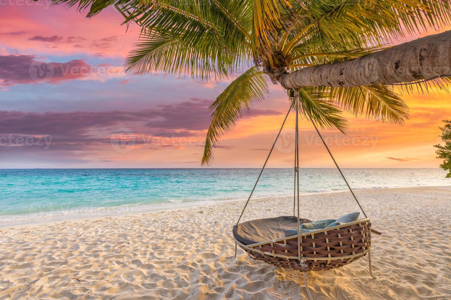 Tropical sunset beach and sky background as exotic summer landscape with beach swing or hammock and white sand and calm sea beach banner. Paradise island beach vacation or summer holiday destination photo