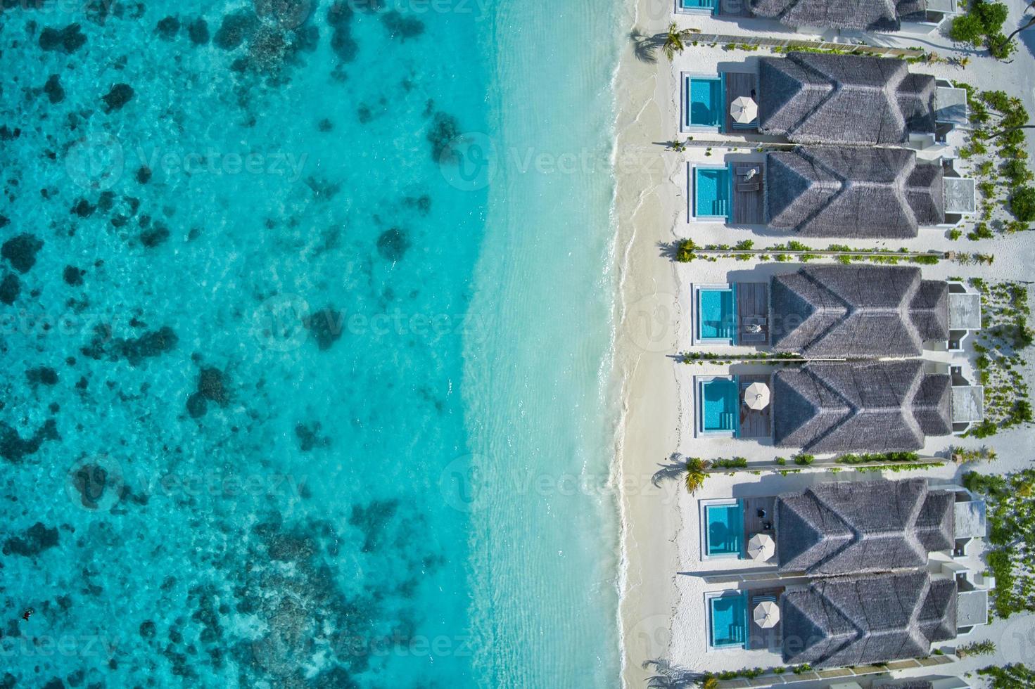 Aerial top view of pool villas, bungalows in Maldives paradise tropical beach. Amazing blue turquoise sea lagoon, ocean bay water. Luxury travel vacation destination. Beautiful sunny aerial landscape photo