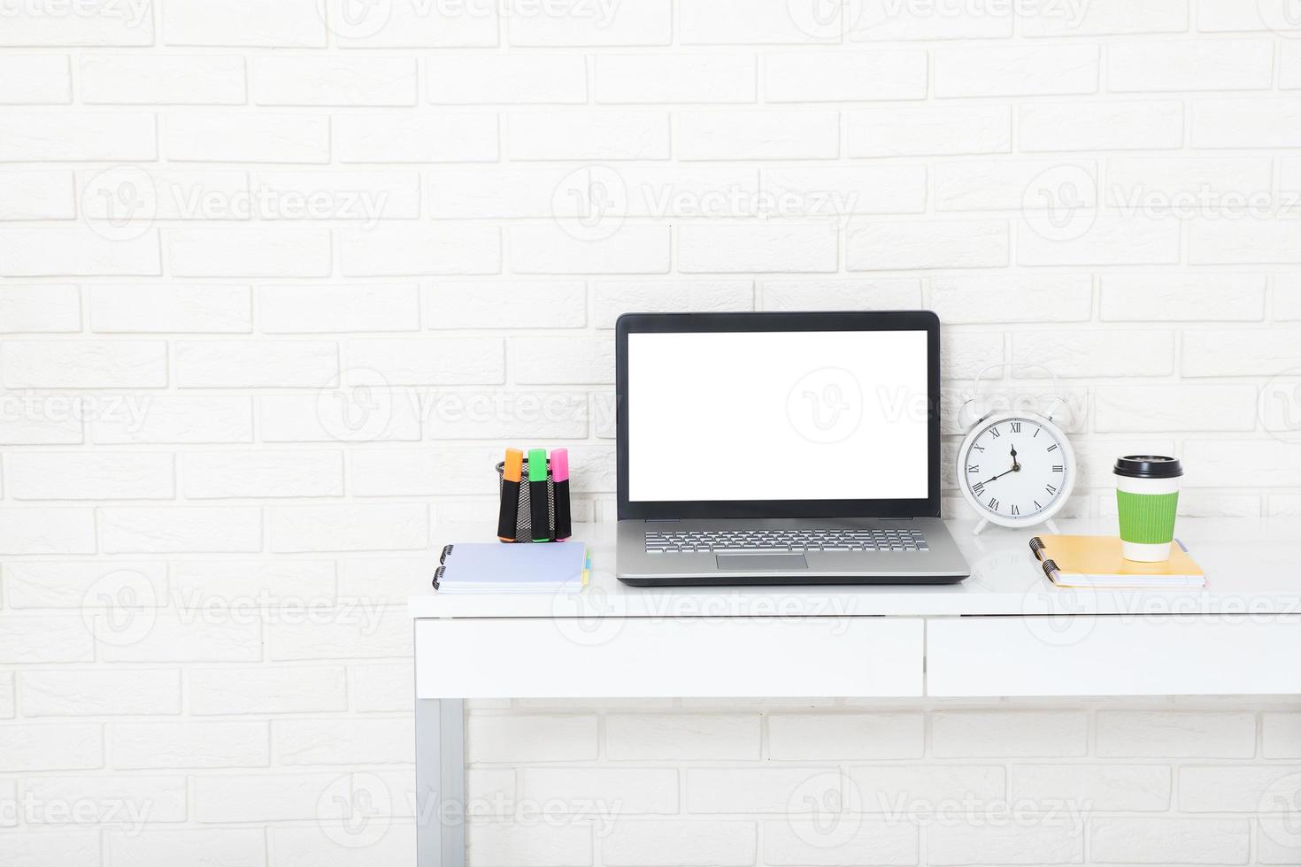 accesorios educativos en la mesa cerca de la pared de ladrillo. computadora vacía y pantalla móvil con lugar para texto. foto