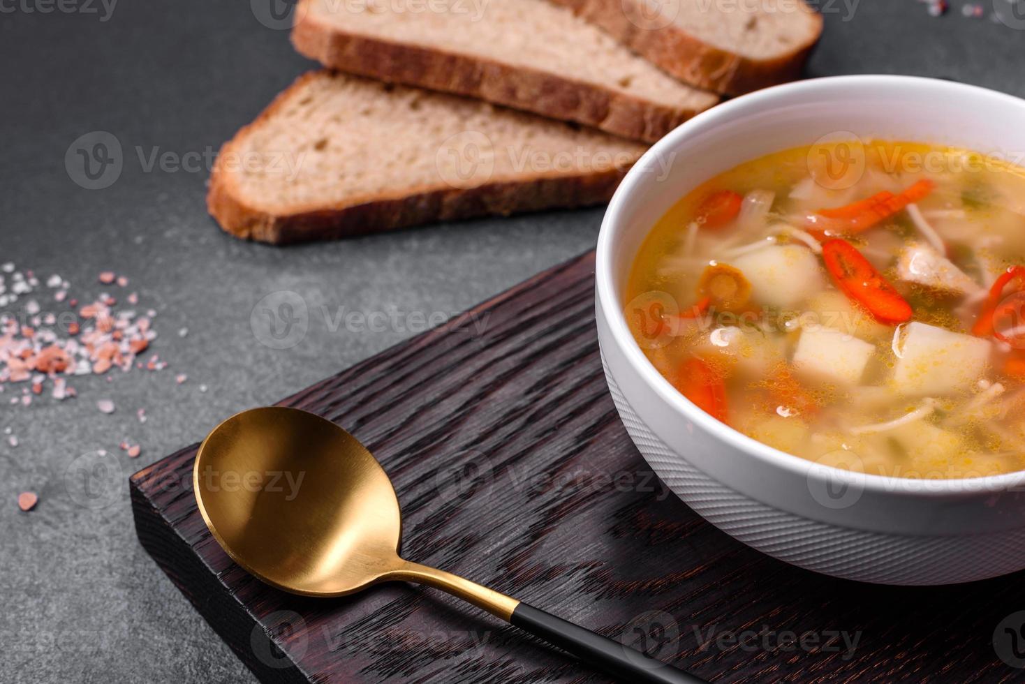 Closeup of a bowl of chicken noodle and vegetable soup on a concrete table photo