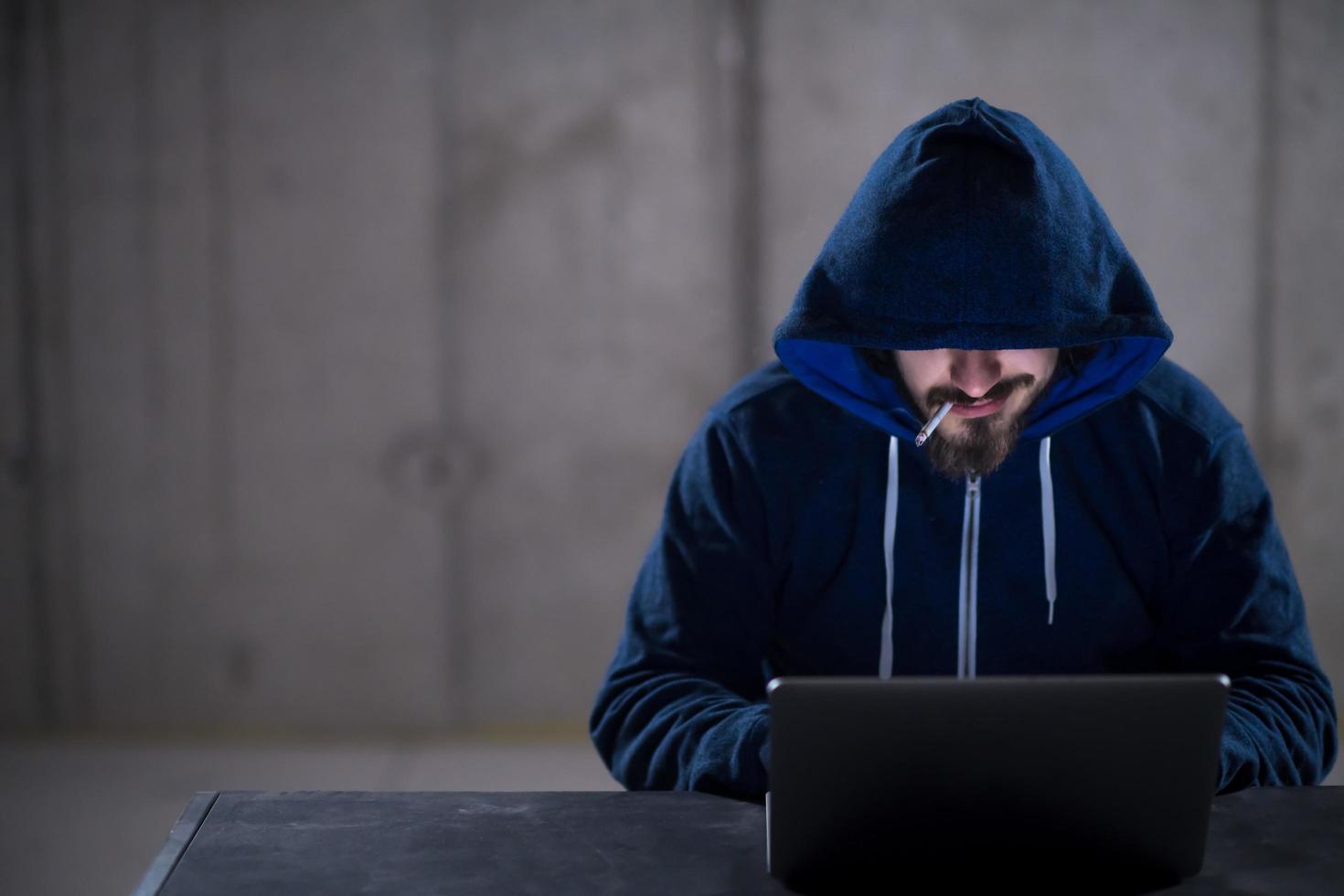 young hacker using laptop computer while working in dark office photo