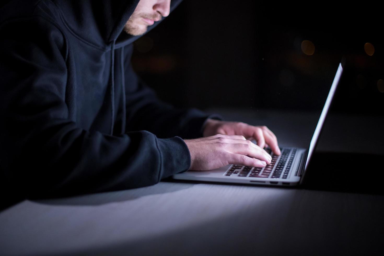 hacker using laptop computer while working in dark office photo