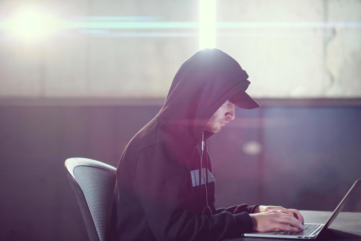 young talented hacker using laptop computer while working in dark office photo