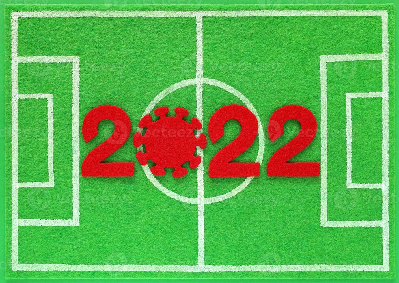 fieltro rojo números de año nuevo 2022, cero en forma de virus corona, colocado en un mini campo de fútbol hecho de fieltro verde, vista superior. concepto sobre el campeonato de fútbol durante la pandemia de covid. foto