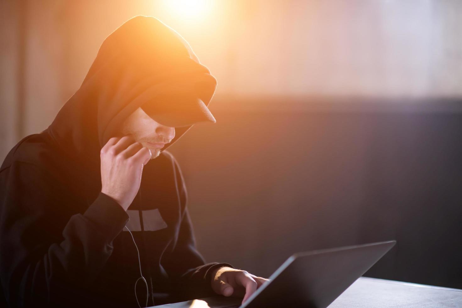 young talented hacker using laptop computer while working in dark office photo