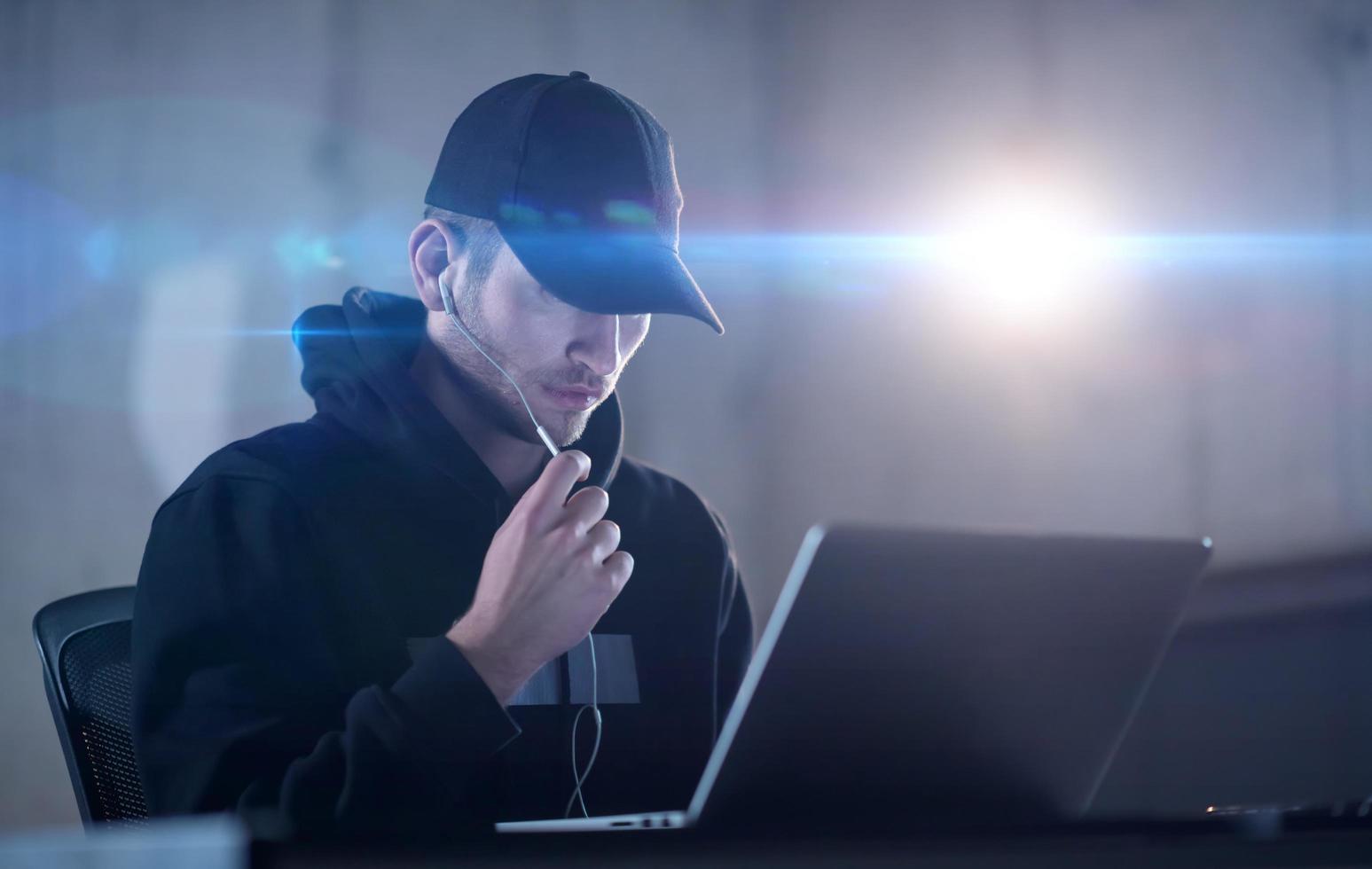 young talented hacker using laptop computer while working in dark office photo