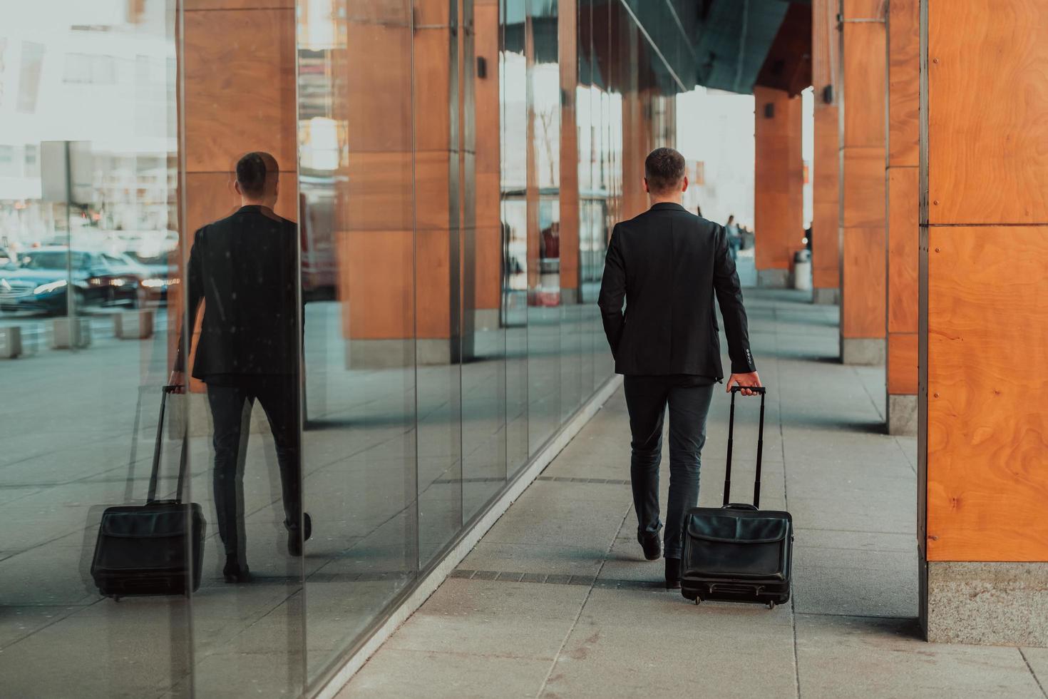 Going to airport terminal. Confident businessman traveler walking on city streets and pulling his suitcase drinking coffee and speaking on smartphone photo