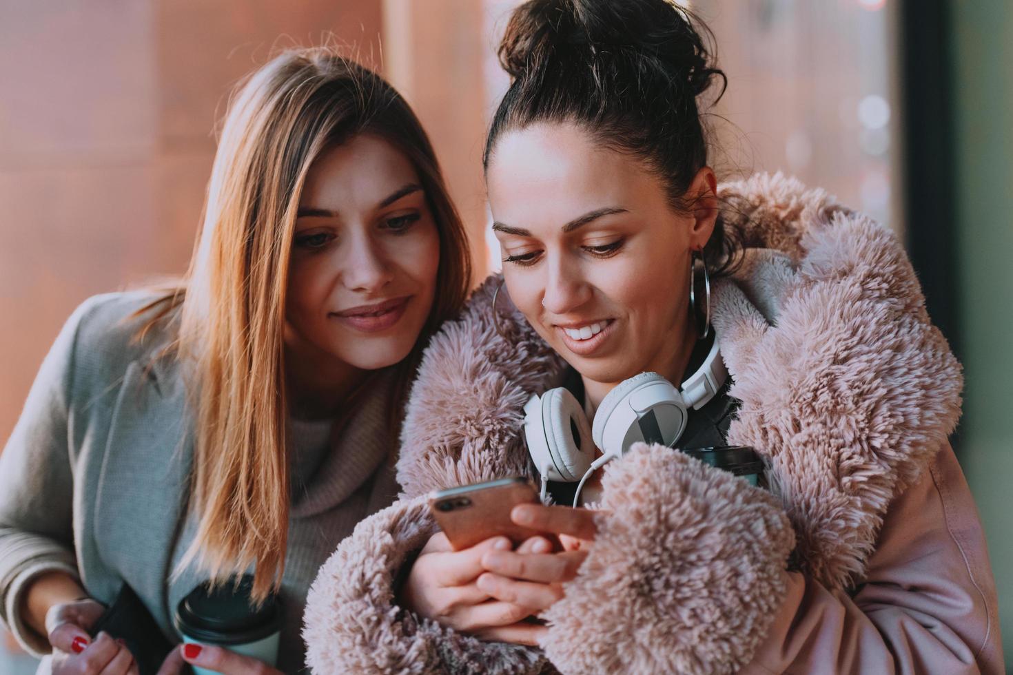 Latino woman with her friend is smiling happily using a smartphone and headphones in the city. photo